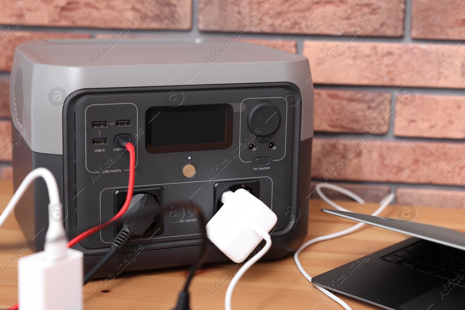 Photo of Laptop charging from portable power station on wooden desk indoors