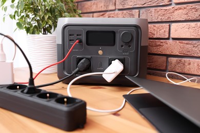 Laptop charging from portable power station on wooden desk indoors