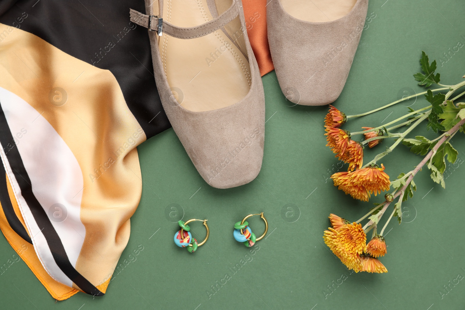 Photo of Pair of ballet flats, earrings, flowers and scarf on green background, flat lay