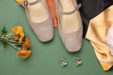 Photo of Pair of ballet flats, earrings, flowers and scarf on green background, flat lay