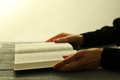 Photo of Woman with open Holy Bible in English language at wooden table, closeup