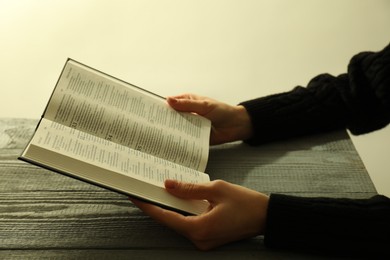 Photo of Woman with open Holy Bible in English language at wooden table, closeup