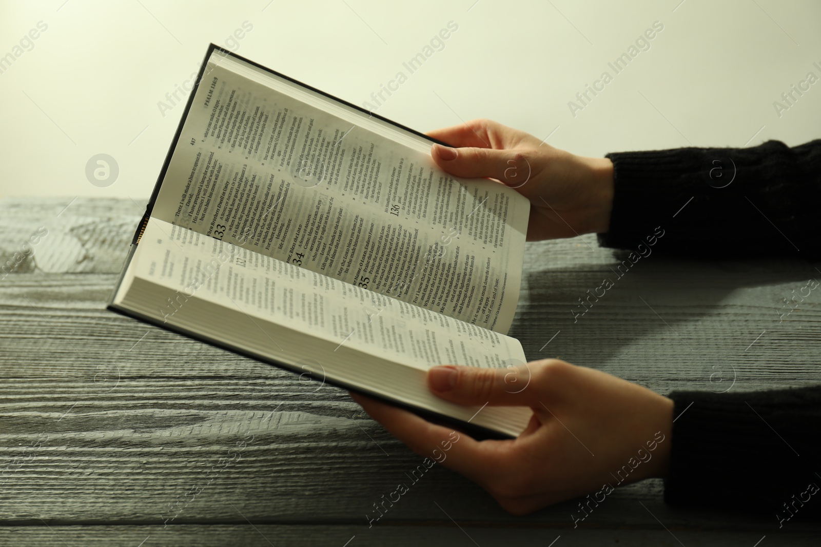 Photo of Woman with open Holy Bible in English language at wooden table, closeup