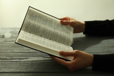 Woman with open Holy Bible in English language at wooden table, closeup