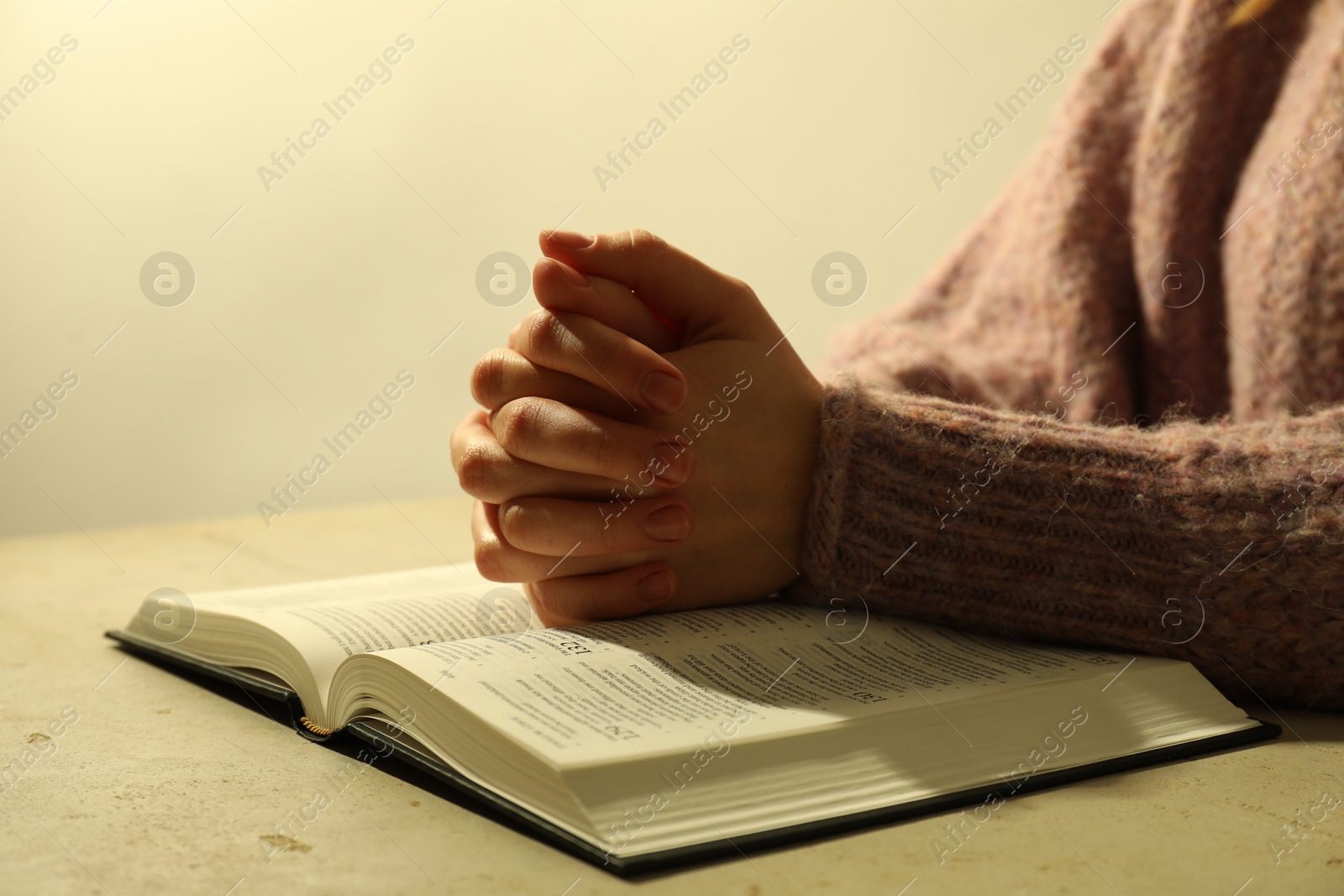 Photo of Woman with open Holy Bible in English language praying at beige table, closeup