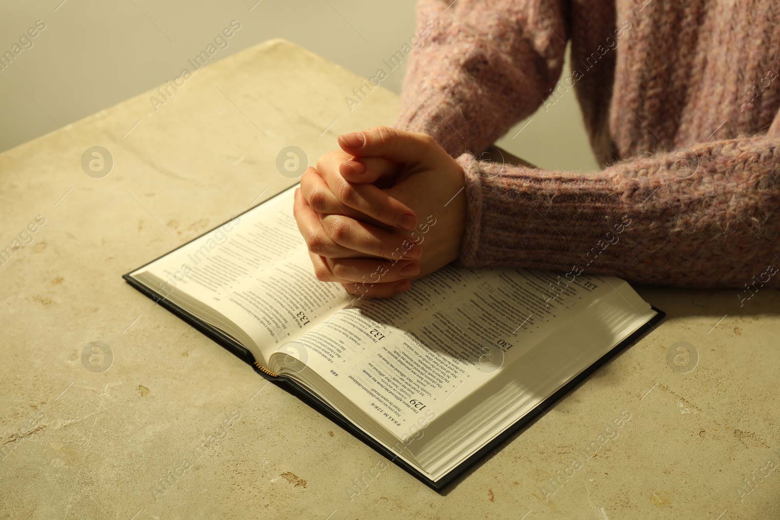 Photo of Woman with open Holy Bible in English language praying at beige table, closeup