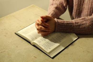 Woman with open Holy Bible in English language praying at beige table, closeup