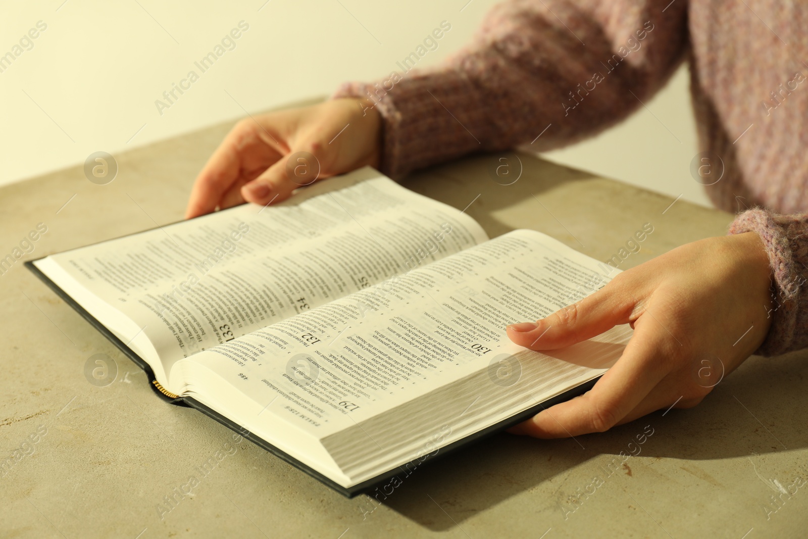 Photo of Woman reading Holy Bible in English language at beige table, closeup