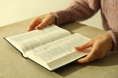 Woman reading Holy Bible in English language at beige table, closeup