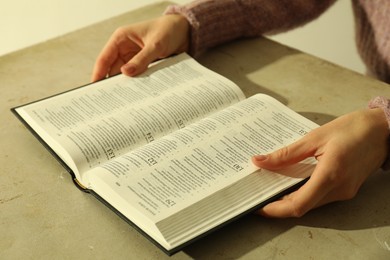 Woman reading Holy Bible in English language at beige table, closeup