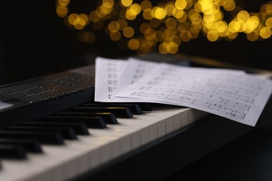 Photo of Sheets with musical notes on piano against blurred lights, closeup. Bokeh effect