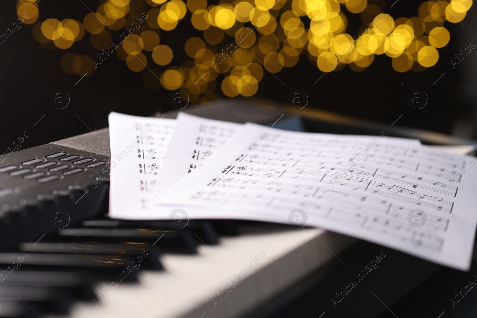 Photo of Sheets with musical notes on piano against blurred lights, closeup. Bokeh effect