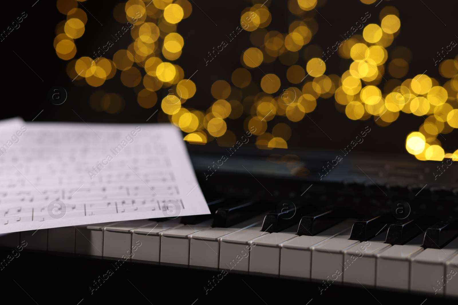 Photo of Sheets with musical notes on piano against blurred lights, closeup. Bokeh effect