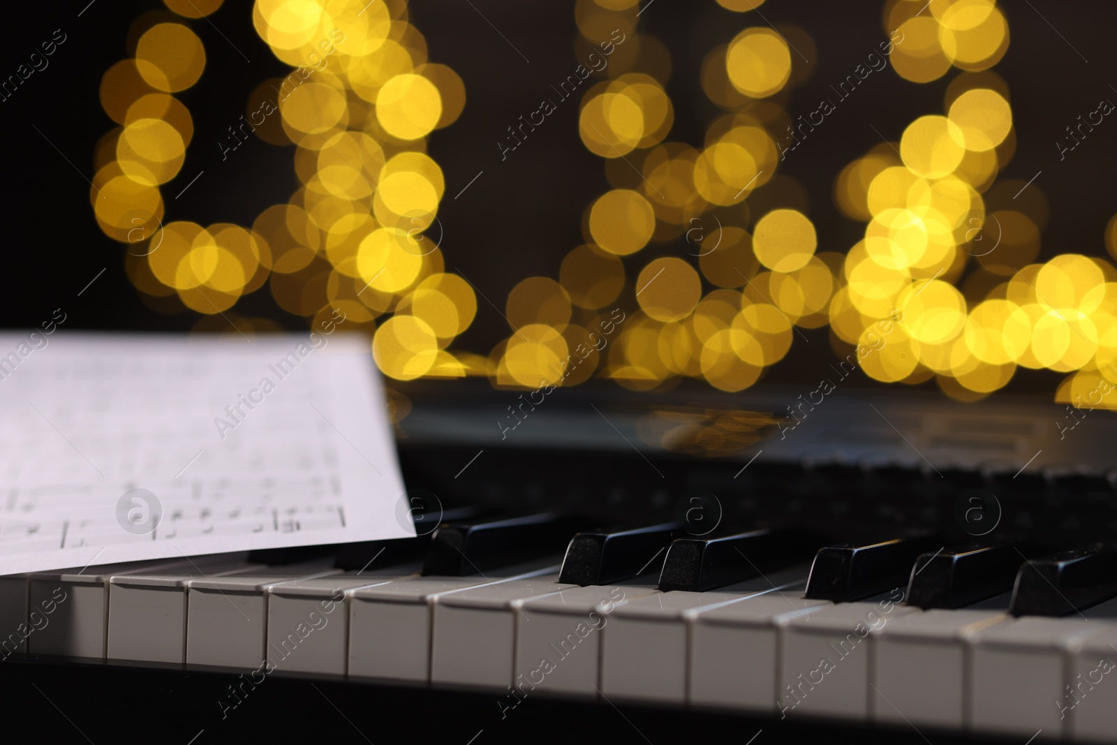 Photo of Sheet with musical notes on piano against blurred lights, closeup. Bokeh effect