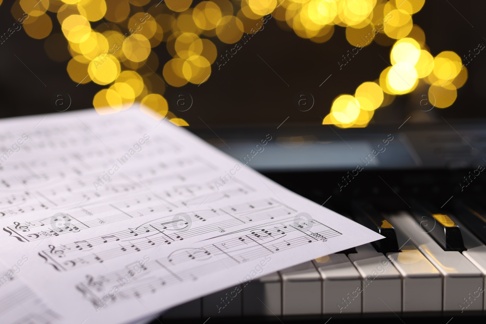 Photo of Sheet with musical notes on piano against blurred lights, closeup. Bokeh effect