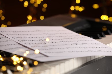 Photo of Sheets with musical notes on piano against blurred lights, closeup. Bokeh effect