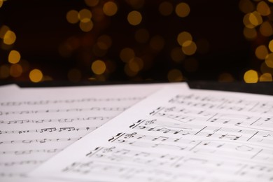 Photo of Sheets of musical notes on table against blurred lights, closeup. Bokeh effect