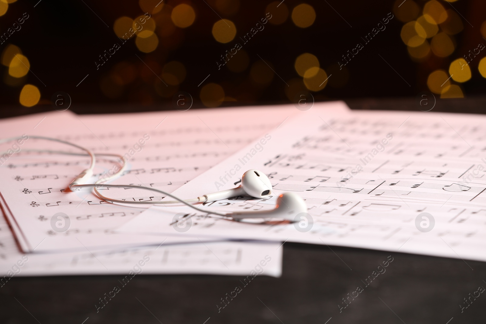 Photo of Sheets of musical notes and earphones on table against blurred lights, closeup. Bokeh effect