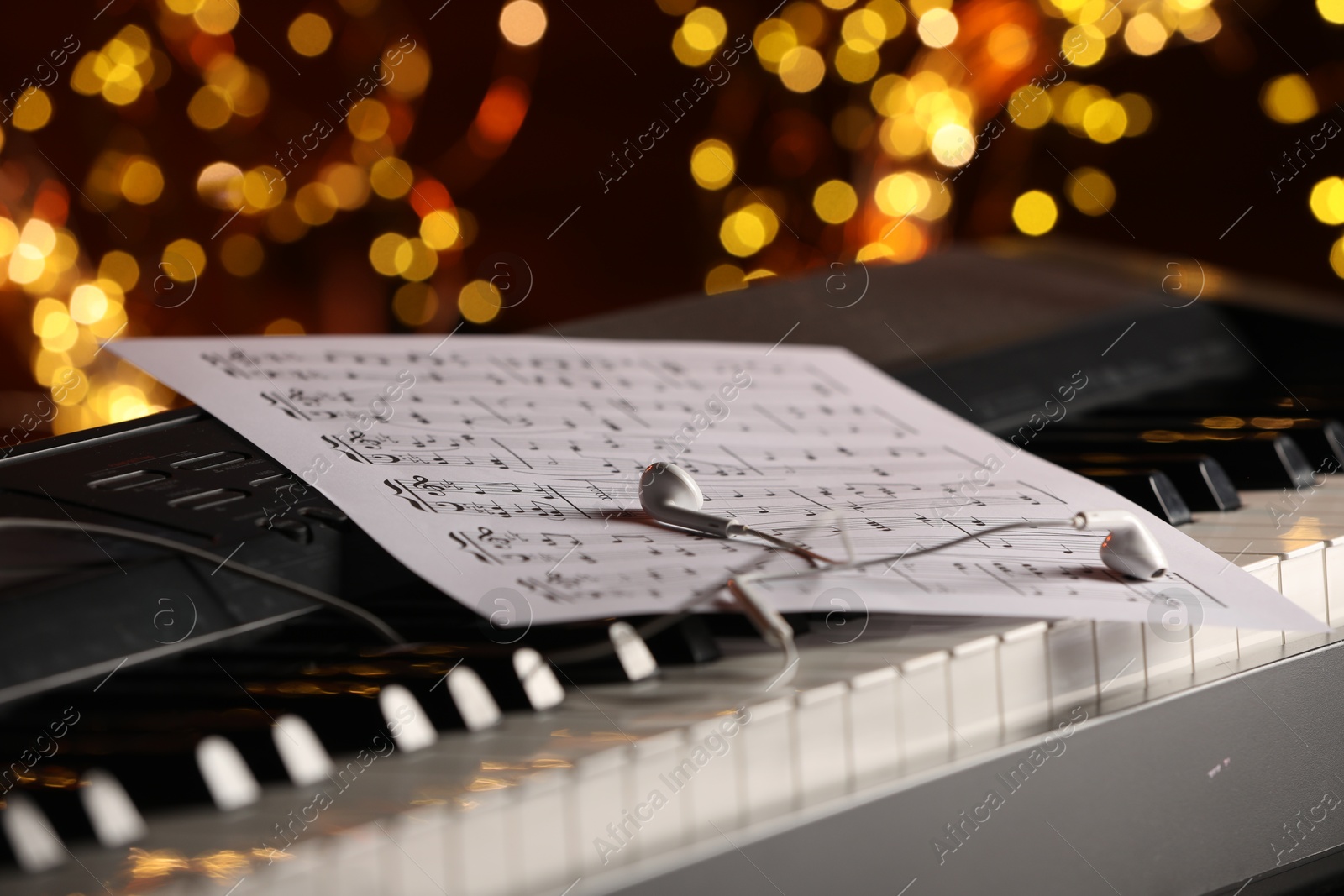 Photo of Sheet with musical notes and earphones on piano against blurred lights, closeup. Bokeh effect