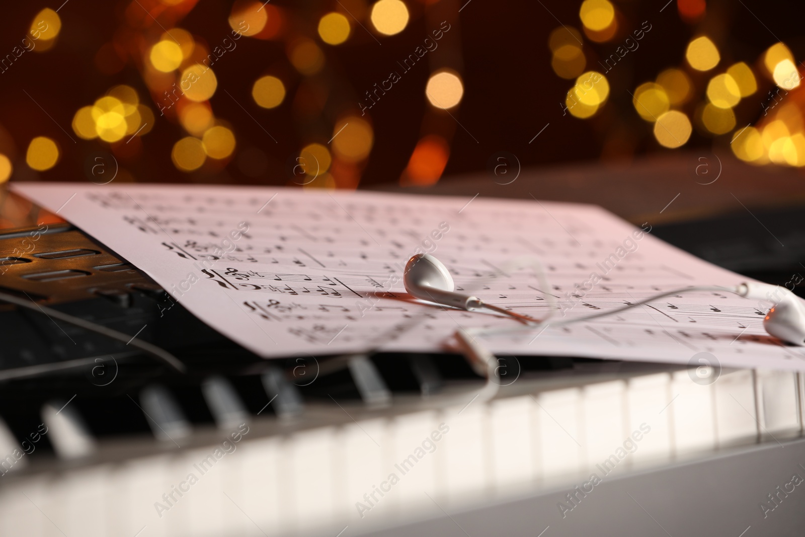 Photo of Sheet with musical notes and earphones on piano against blurred lights, closeup. Bokeh effect