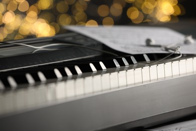 Photo of Sheet with musical notes and earphones on piano against blurred lights, closeup. Bokeh effect