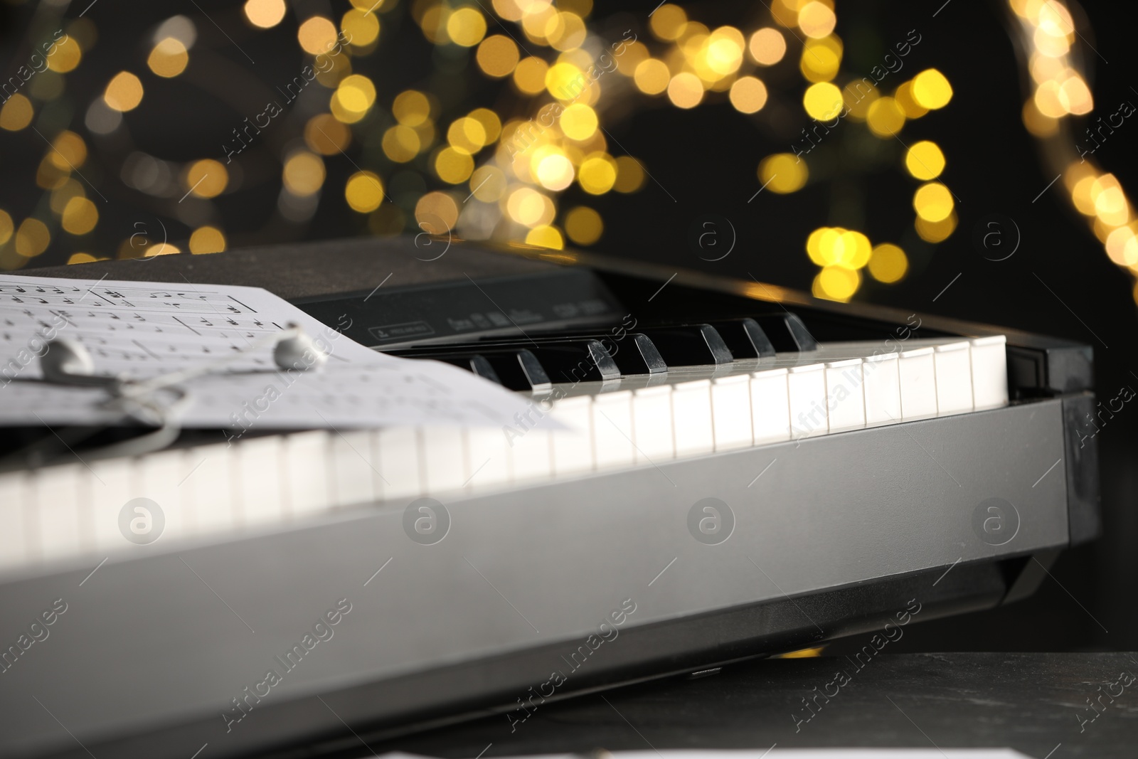 Photo of Sheet with musical notes and earphones on piano against blurred lights, closeup. Bokeh effect