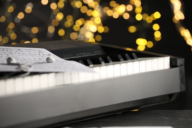 Photo of Sheet with musical notes and earphones on piano against blurred lights, closeup. Bokeh effect