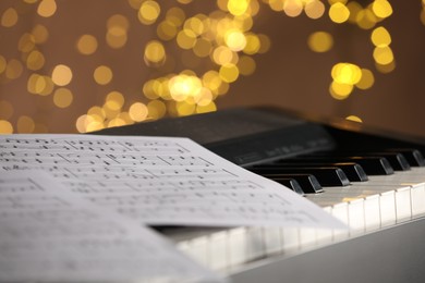 Photo of Sheets with musical notes on piano against blurred lights, closeup. Bokeh effect