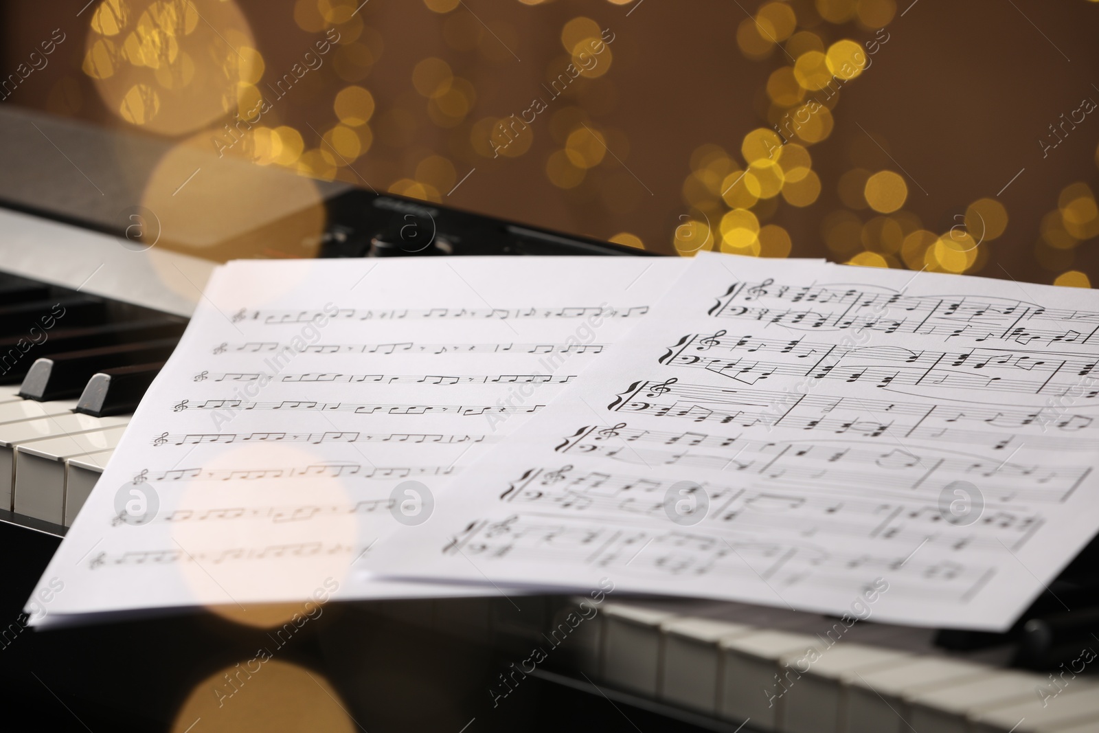 Photo of Sheets with musical notes on piano against blurred lights, closeup. Bokeh effect