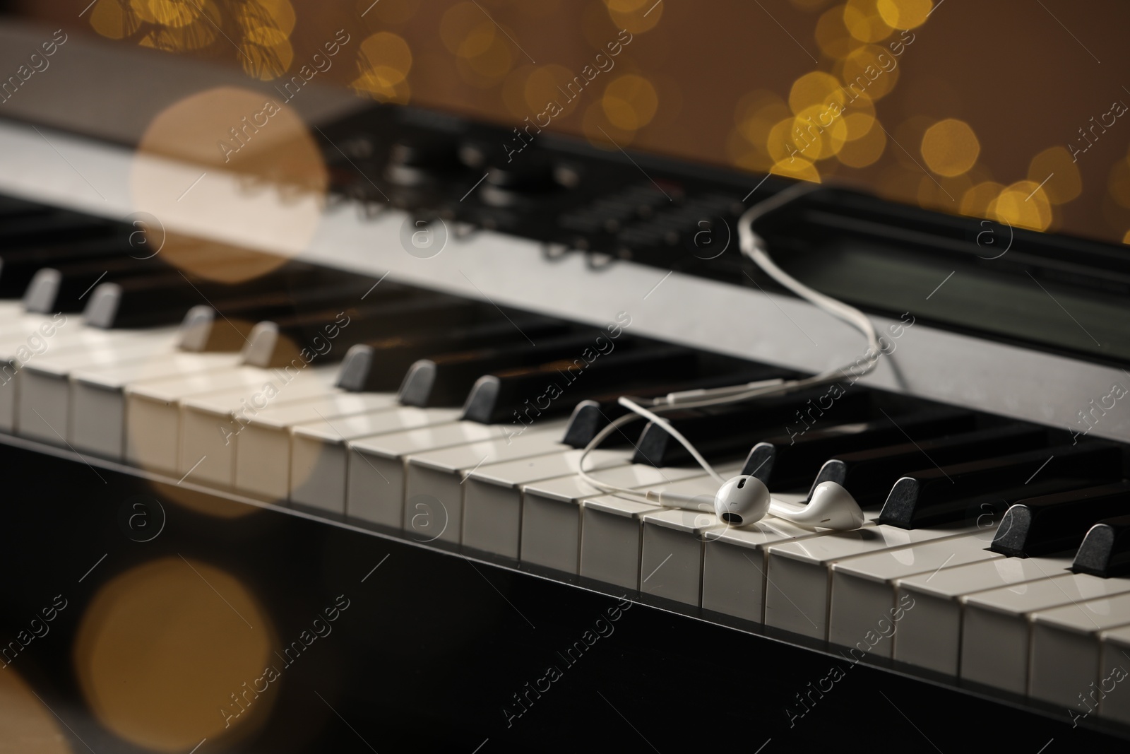 Photo of Earphones on piano against blurred lights, closeup. Bokeh effect