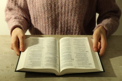 Photo of Woman reading Holy Bible in English language at beige table, closeup