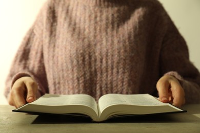 Photo of Woman reading Holy Bible in English language at beige table, closeup