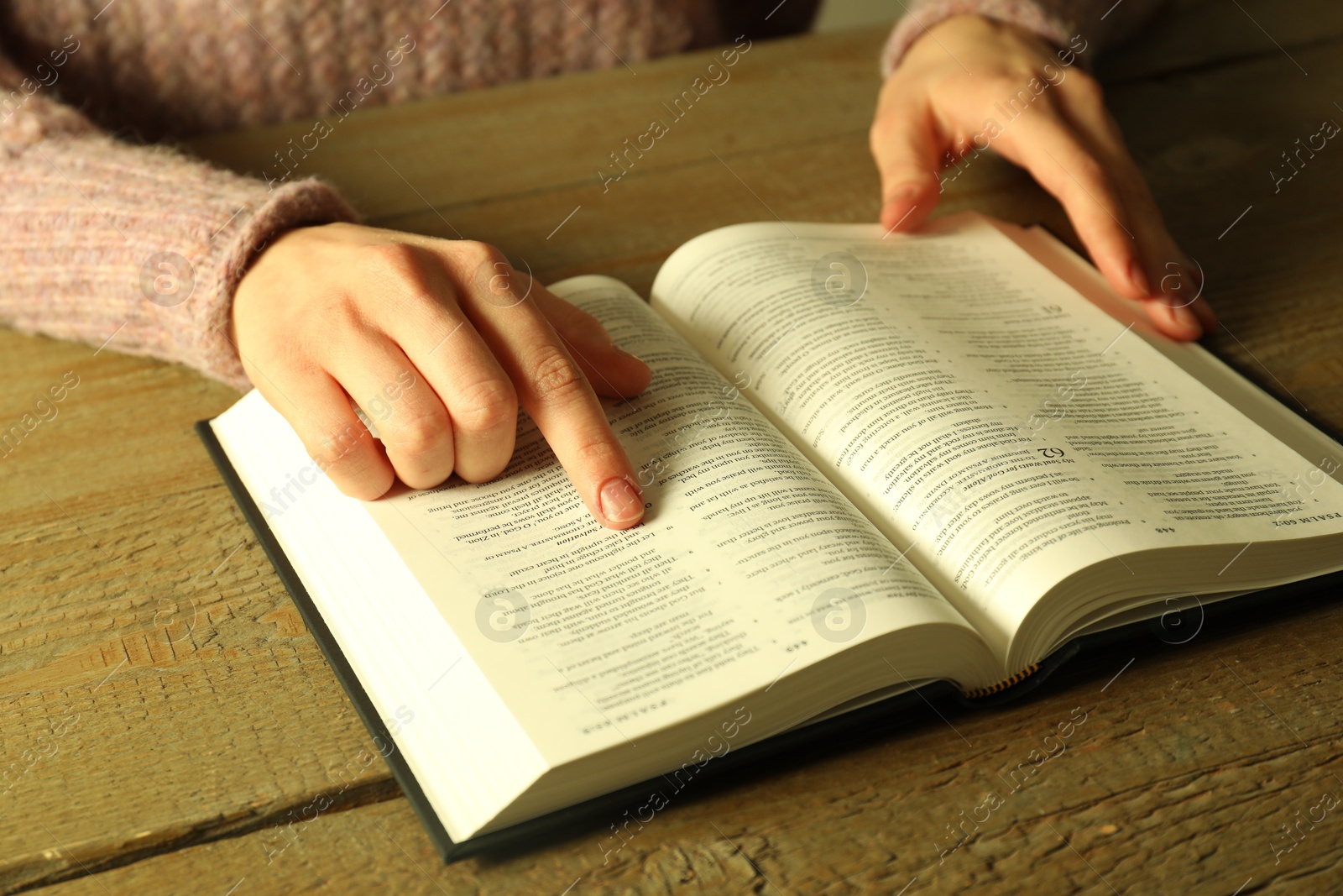 Photo of Woman reading Holy Bible in English language at wooden table, closeup