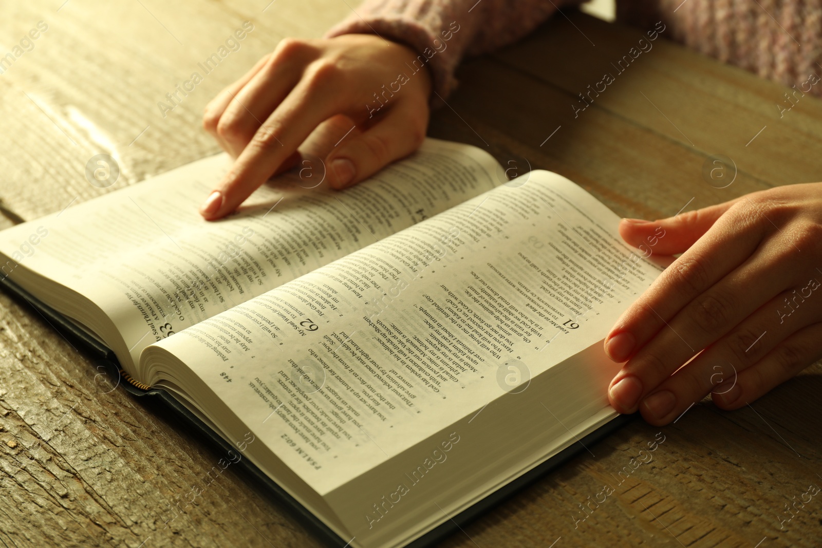 Photo of Woman reading Holy Bible in English language at wooden table, closeup