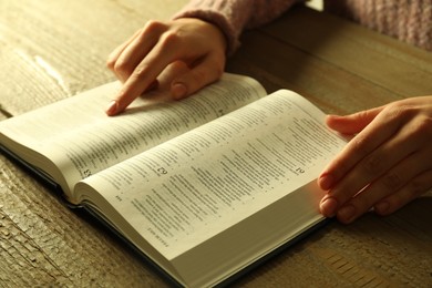 Woman reading Holy Bible in English language at wooden table, closeup