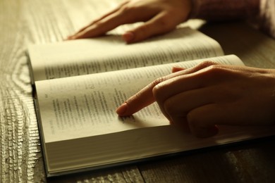 Photo of Woman reading Holy Bible in English language at wooden table, closeup