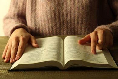 Woman reading Holy Bible in English language at wooden table, closeup