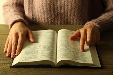 Photo of Woman reading Holy Bible in English language at wooden table, closeup