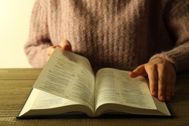 Woman reading Holy Bible in English language at wooden table, closeup