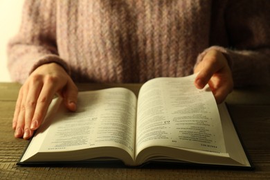 Photo of Woman reading Holy Bible in English language at wooden table, closeup