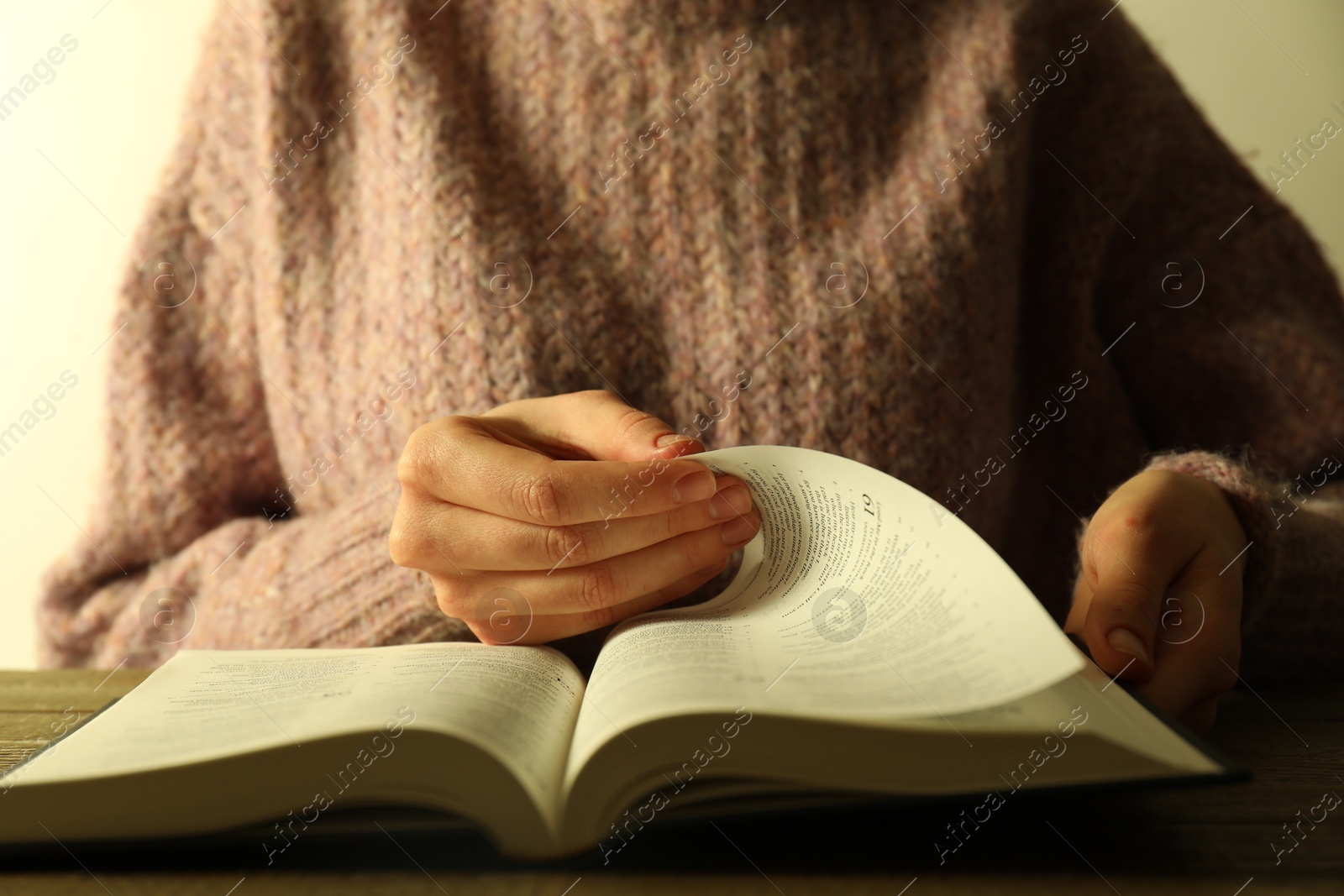 Photo of Woman reading Holy Bible in English language at wooden table, closeup