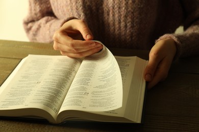 Woman reading Holy Bible in English language at wooden table, closeup