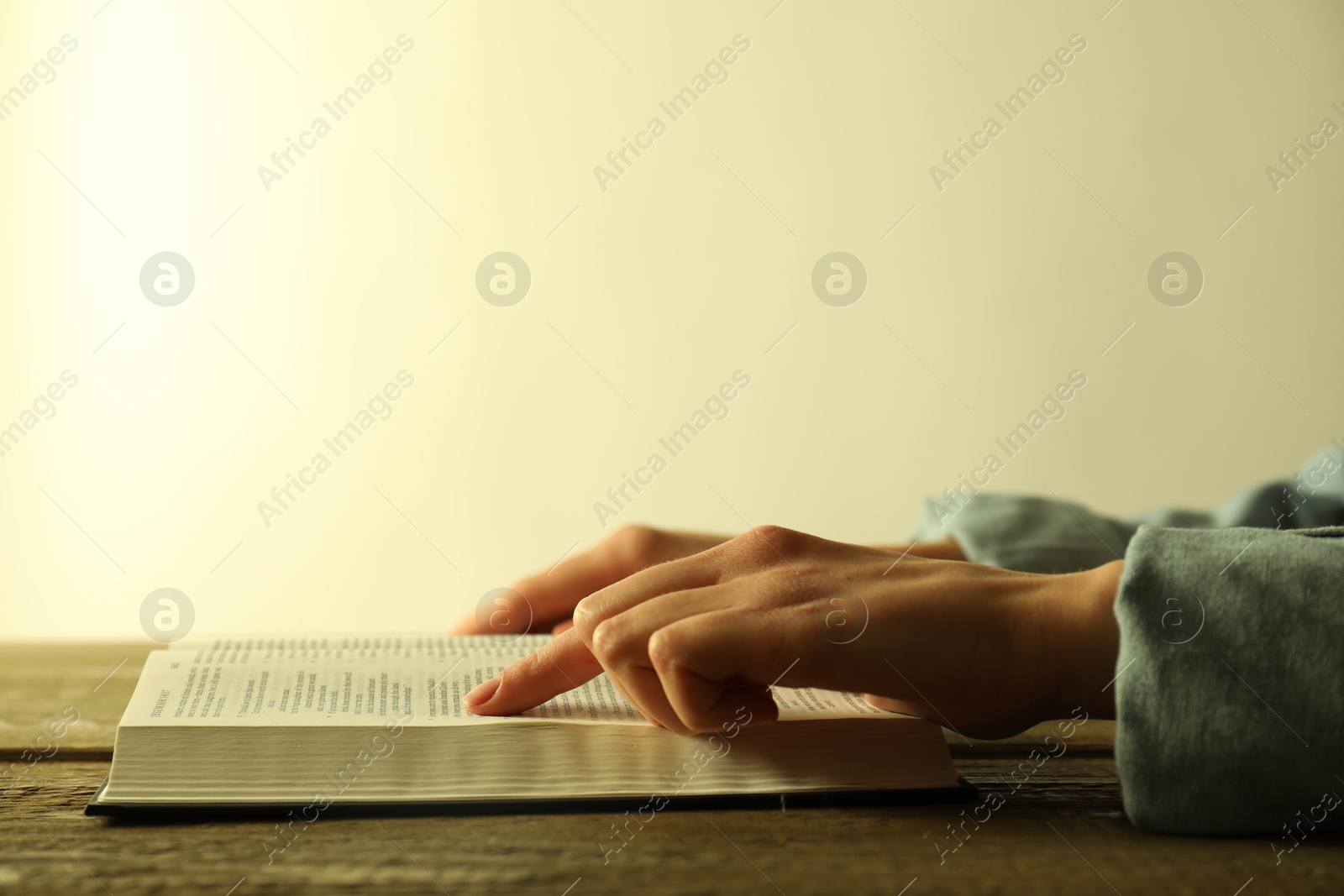 Photo of Woman reading Holy Bible in English language at wooden table, closeup