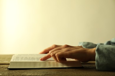 Woman reading Holy Bible in English language at wooden table, closeup