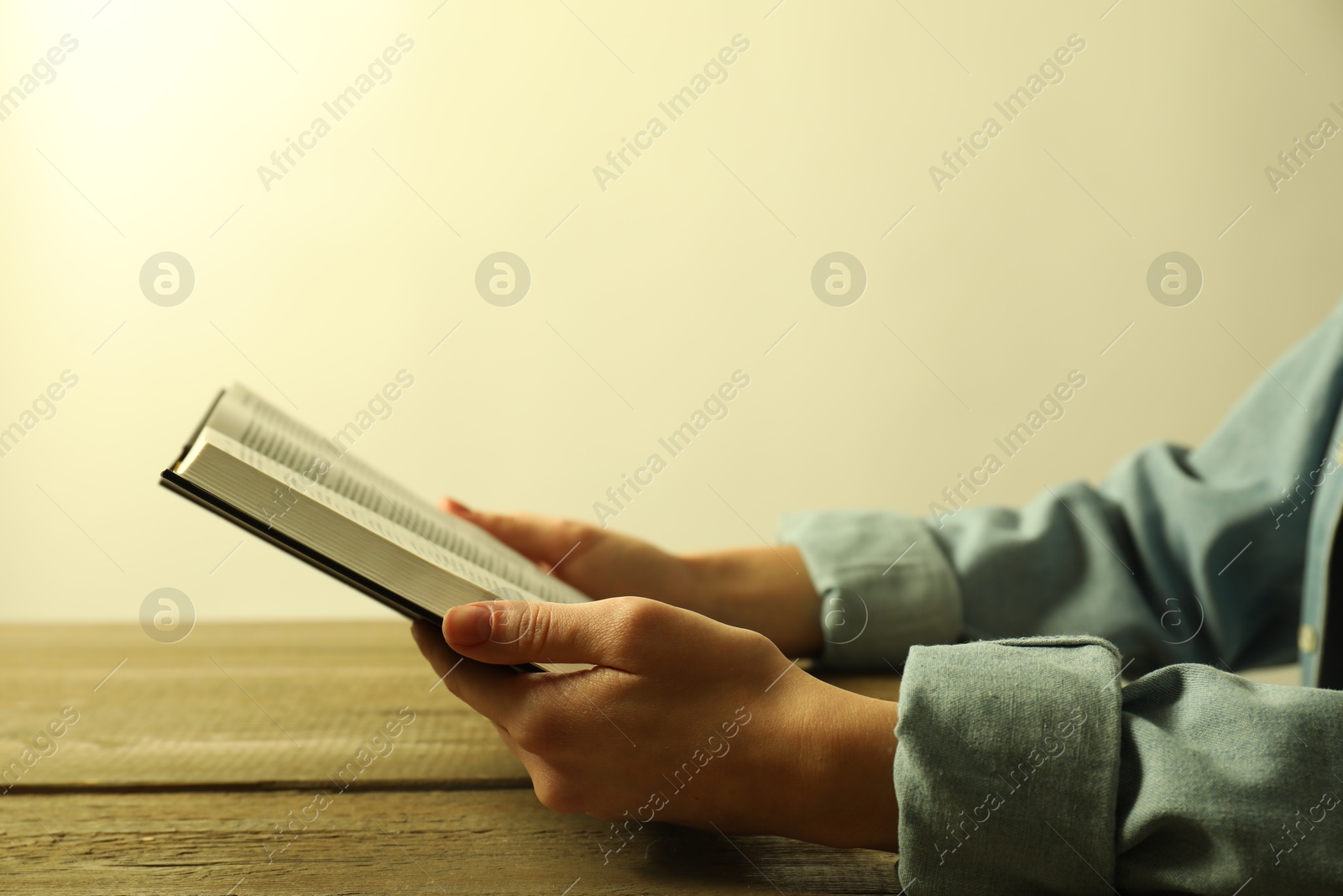 Photo of Woman reading Holy Bible at wooden table, closeup