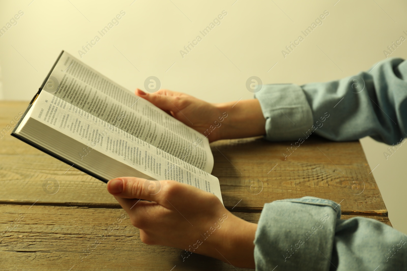 Photo of Woman reading Holy Bible in English language at wooden table, closeup