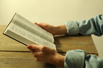 Woman reading Holy Bible in English language at wooden table, closeup