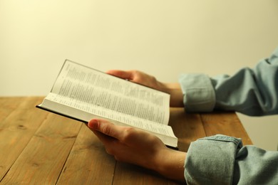 Woman reading Holy Bible in English language at wooden table, closeup