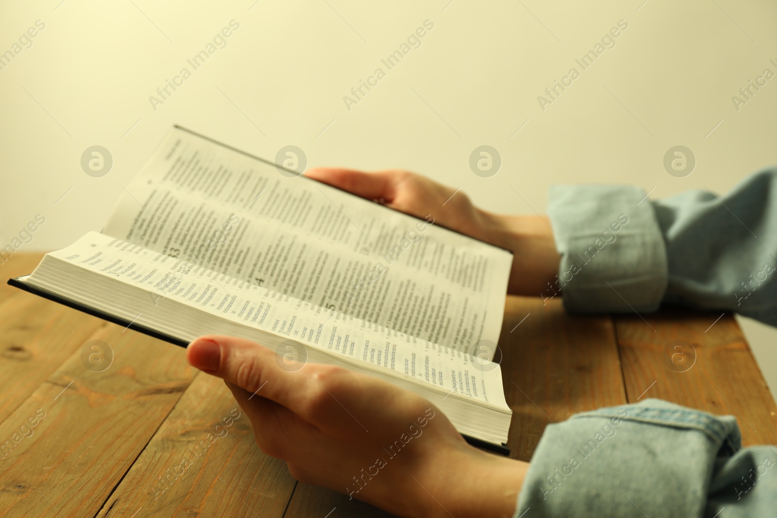 Photo of Woman reading Holy Bible in English language at wooden table, closeup