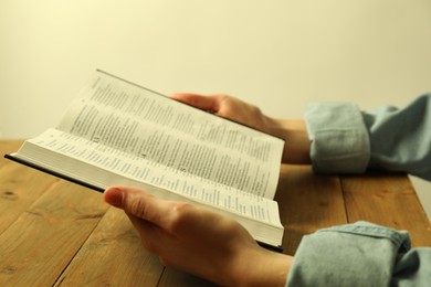 Photo of Woman reading Holy Bible in English language at wooden table, closeup